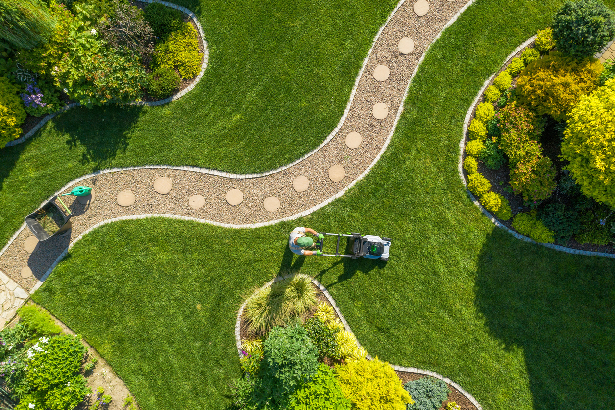 Aerial view of a gardener trimming the grass in a very spacious yard.